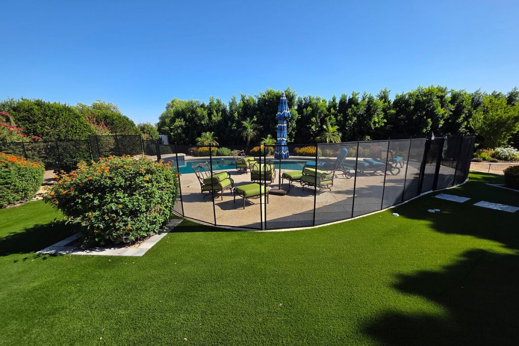 Removable mesh pool fence separating a turf lawn from a pool patio